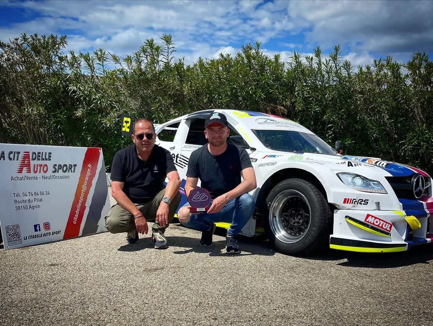 Nicolas et Bastien Buisson accroupis devant une voiture de course n°52 et le panneau La Citadelle Auto Sport, Bastien tenant un trophée
